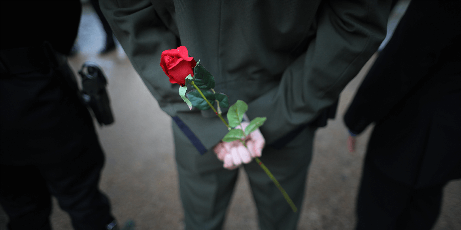 Three law enforcement officers stand next to one another with hands clasped behind their backs. One is holding a single rose.