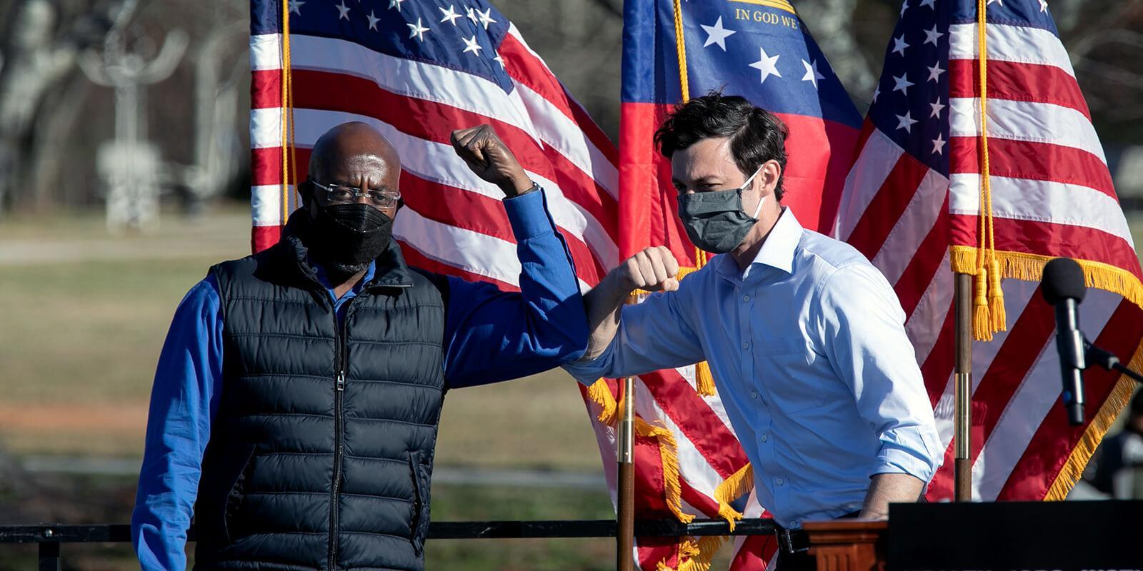 Democratic U.S. Senate candidates Raphael Warnock (L) and Jon Ossoff bump elbows during an outdoor drive-in rally in Conyers, Georgia.